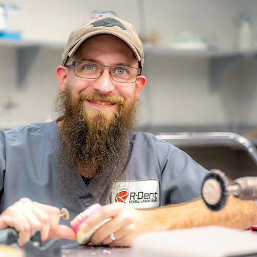 R-Dent technician smiling at the camera and working on a denture.